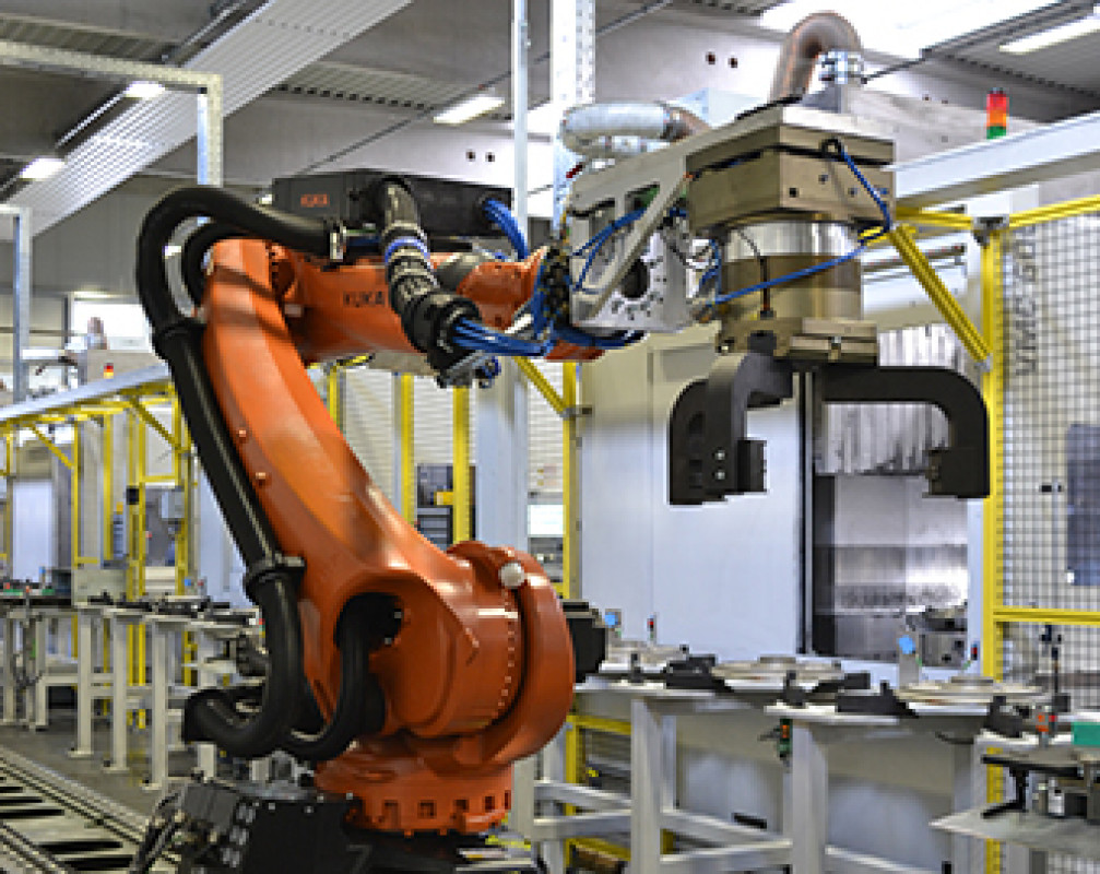 KUKA-Roboter mit einem Schwungrad im Greifer. Die Gussteile durchlaufen mehrere Stationen, bis sie einbaufertig sind. Dabei werden sie induktiv bearbeitet, gewuchtet, gewaschen und gekennzeichnet. - © M. Busch KUKA-Roboter mit einem Schwungrad im Greifer. Die Gussteile durchlaufen mehrere Stationen, bis sie einbaufertig sind. Dabei werden sie induktiv bearbeitet, gewuchtet, gewaschen und gekennzeichnet. - © M. Busch